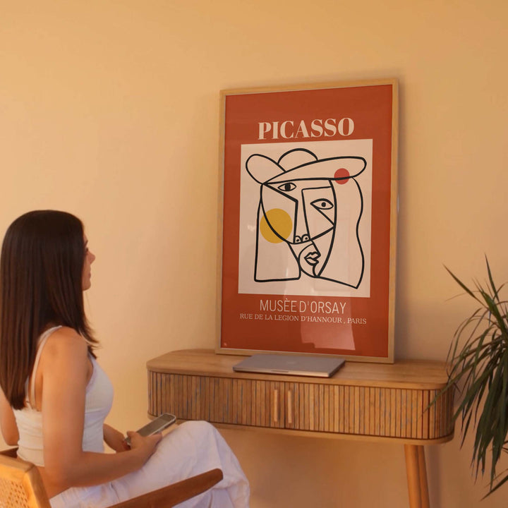 Woman sitting on a chair looking at a Picasso poster on a wall.